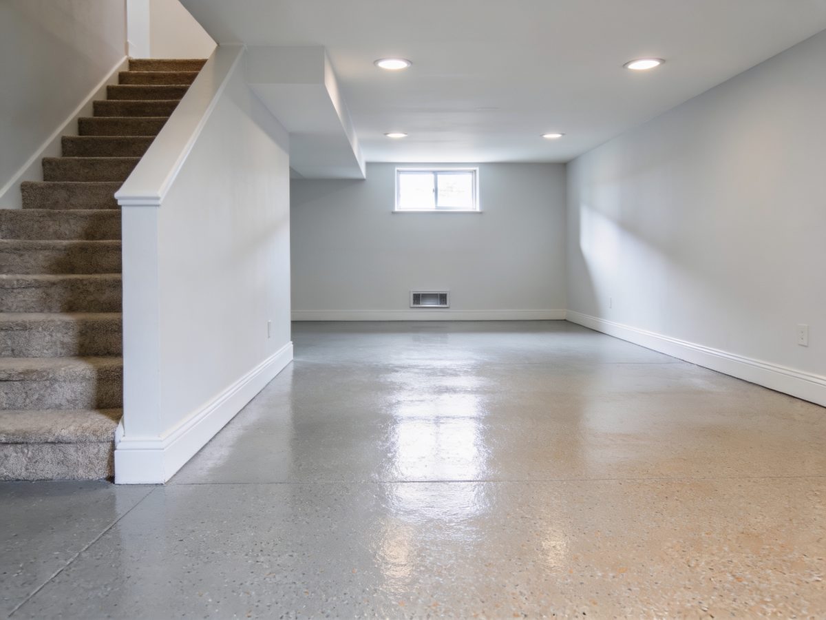 A finished basement lower level with a light flake floor coating and stairs descending into the room